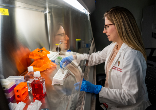 Dr. Hilary Faust in a white lab coat working under a lab hood